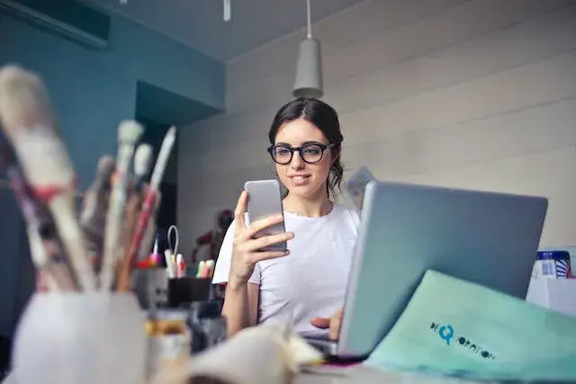 Young woman looking at her cellphone in front of the computer.